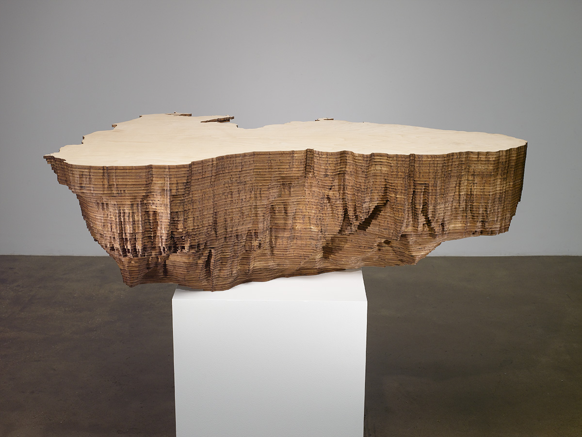 Large wood sculpture on a pedestal that looks like a topographical  landscape