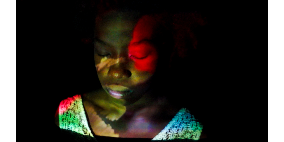 Still fom movie with abstract image of a woman in foreground with colorful sleeveless shirt and reflection on her face