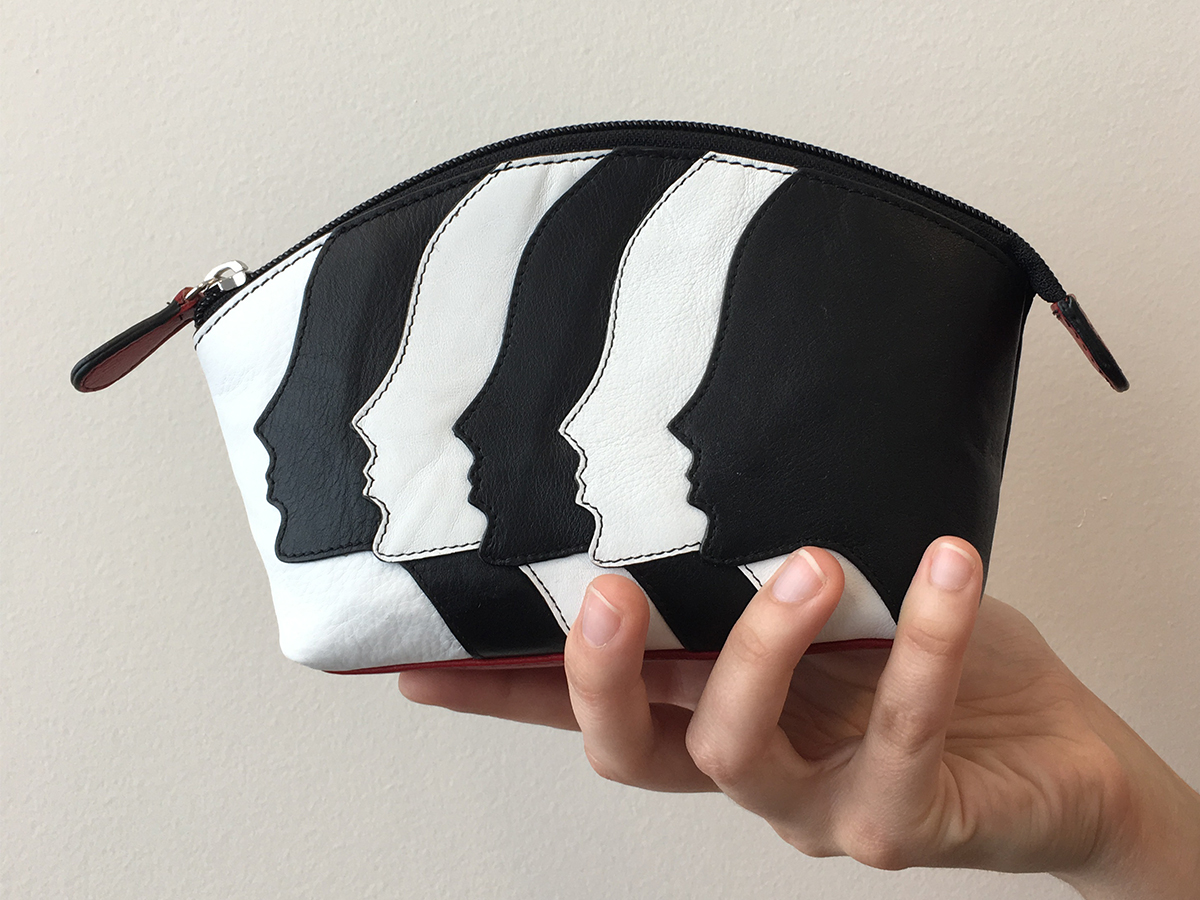 Photo of a hand holding a small black and white purse with face silhouettes on the purse