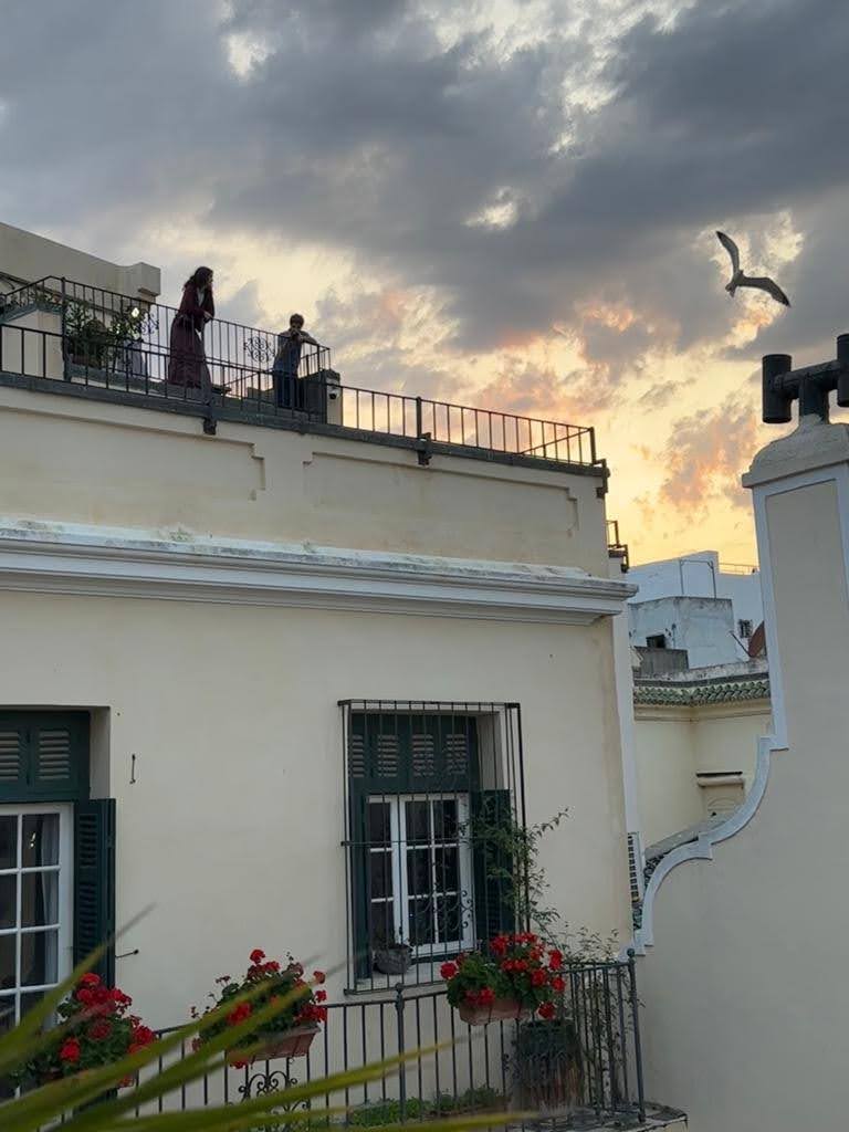 View of a museum facade with two people visible at the top looking out from a rooftop terrace.