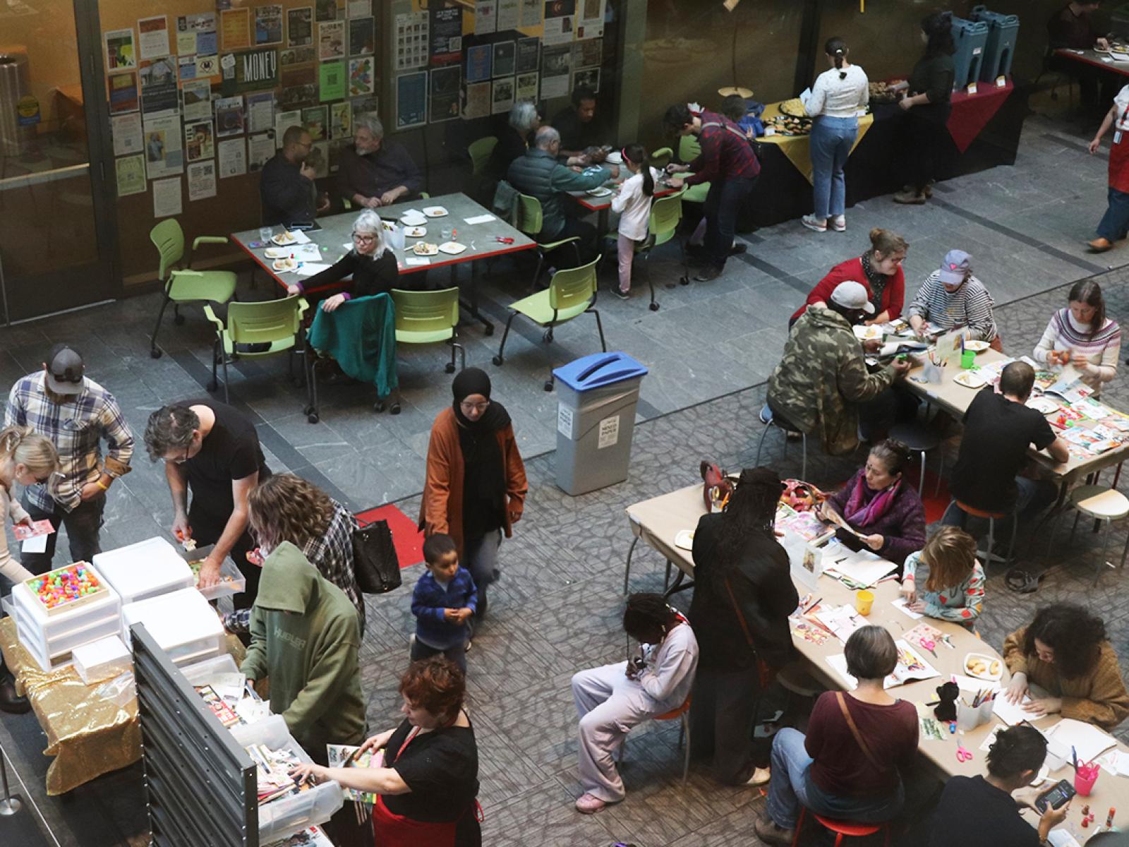 bird's eye view of an atrium full of about 32 people of all ages making art at tables and eating refreshments