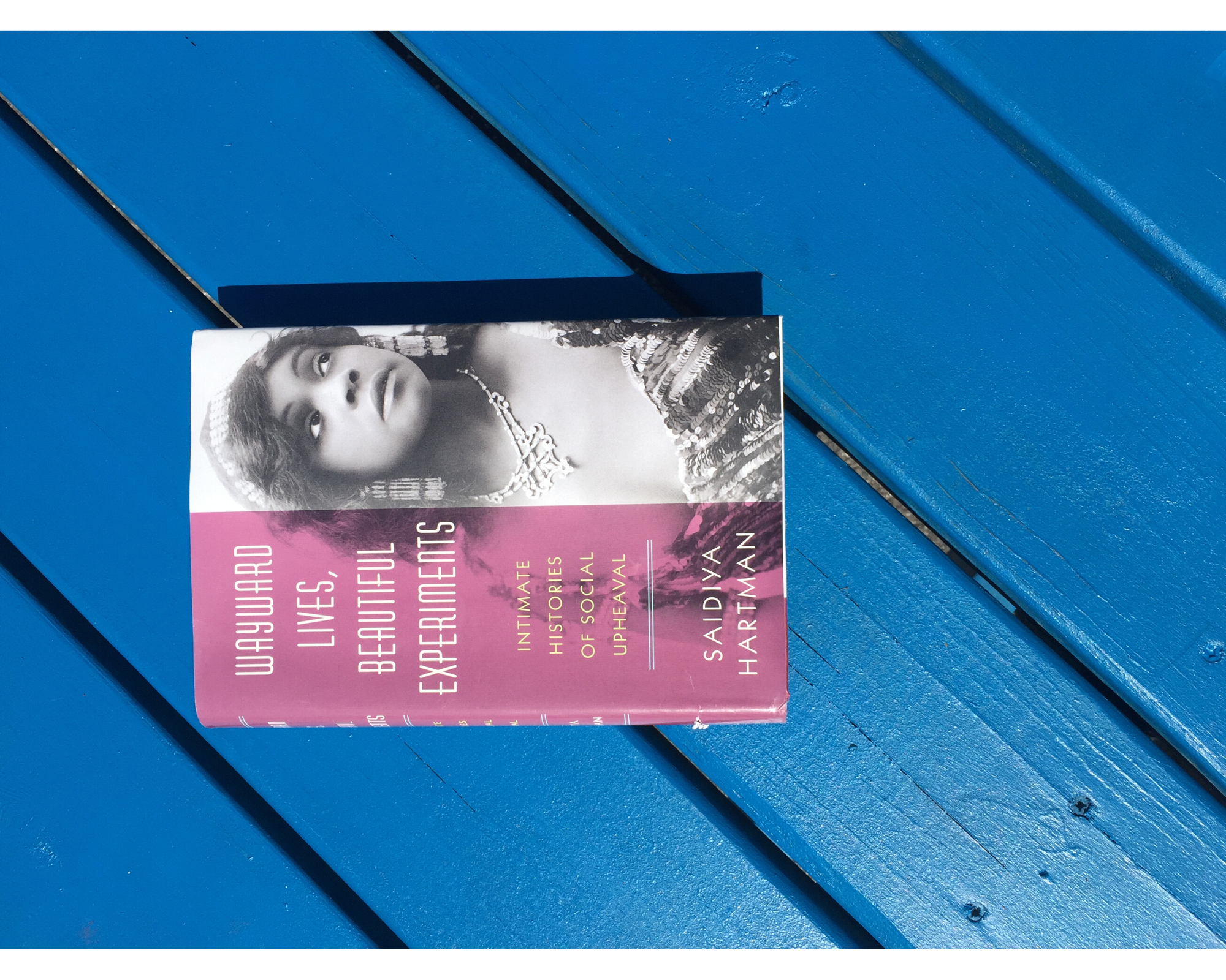 Saidiya Hartman's book "Wayward Lives, Beautiful Experiments: Intimate Histories of Social Upheaval" resting on a blue tabletop