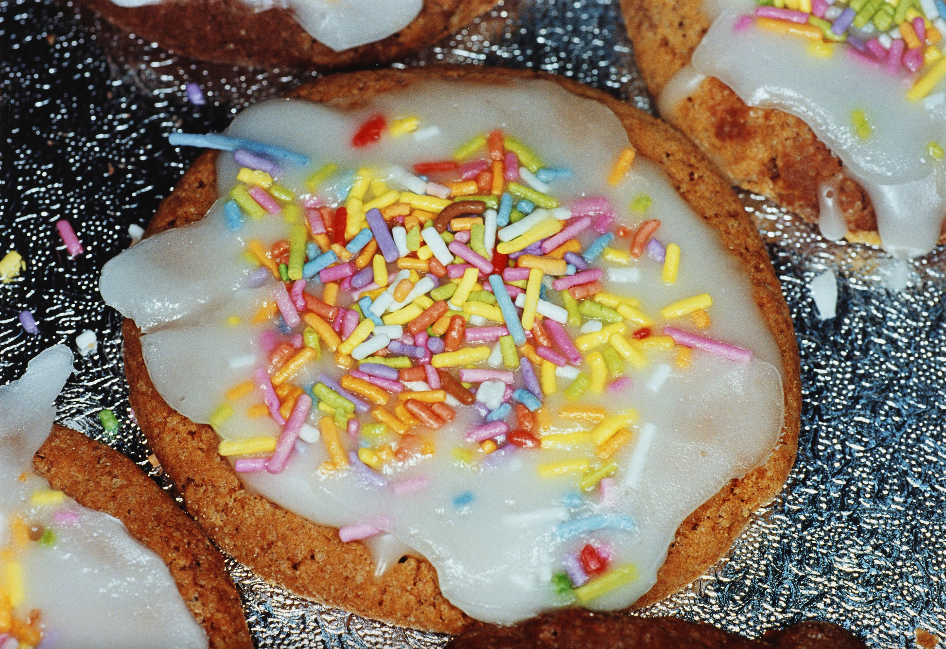 Close up of cookie with frosting and rainbow sprinkles by Martin Parr. 