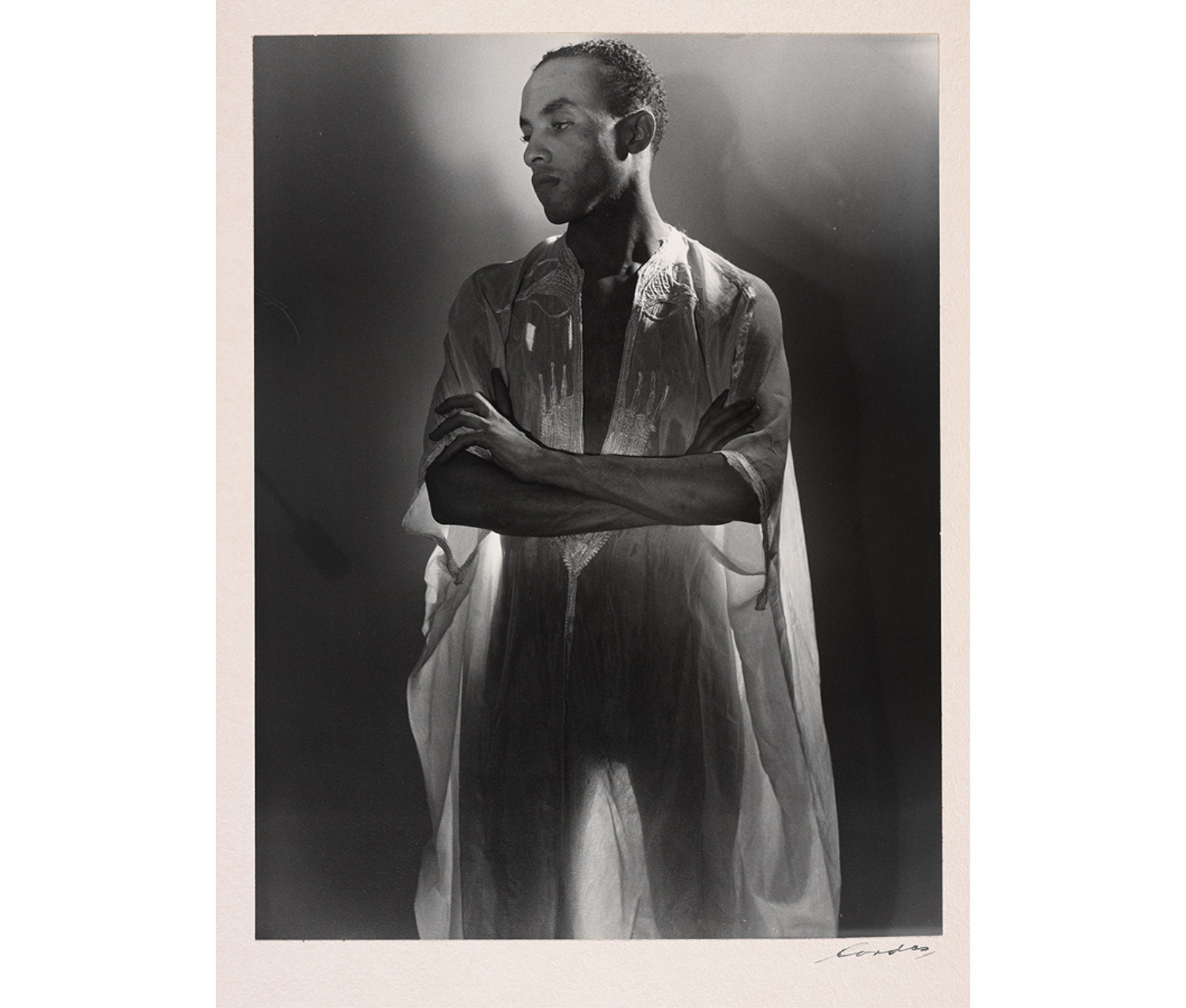 Three-quarter portrait of a Black man in a translucent gown. The lighting is dramatic; his arms are crossed and he looks to the bottom left corner of the portrait.