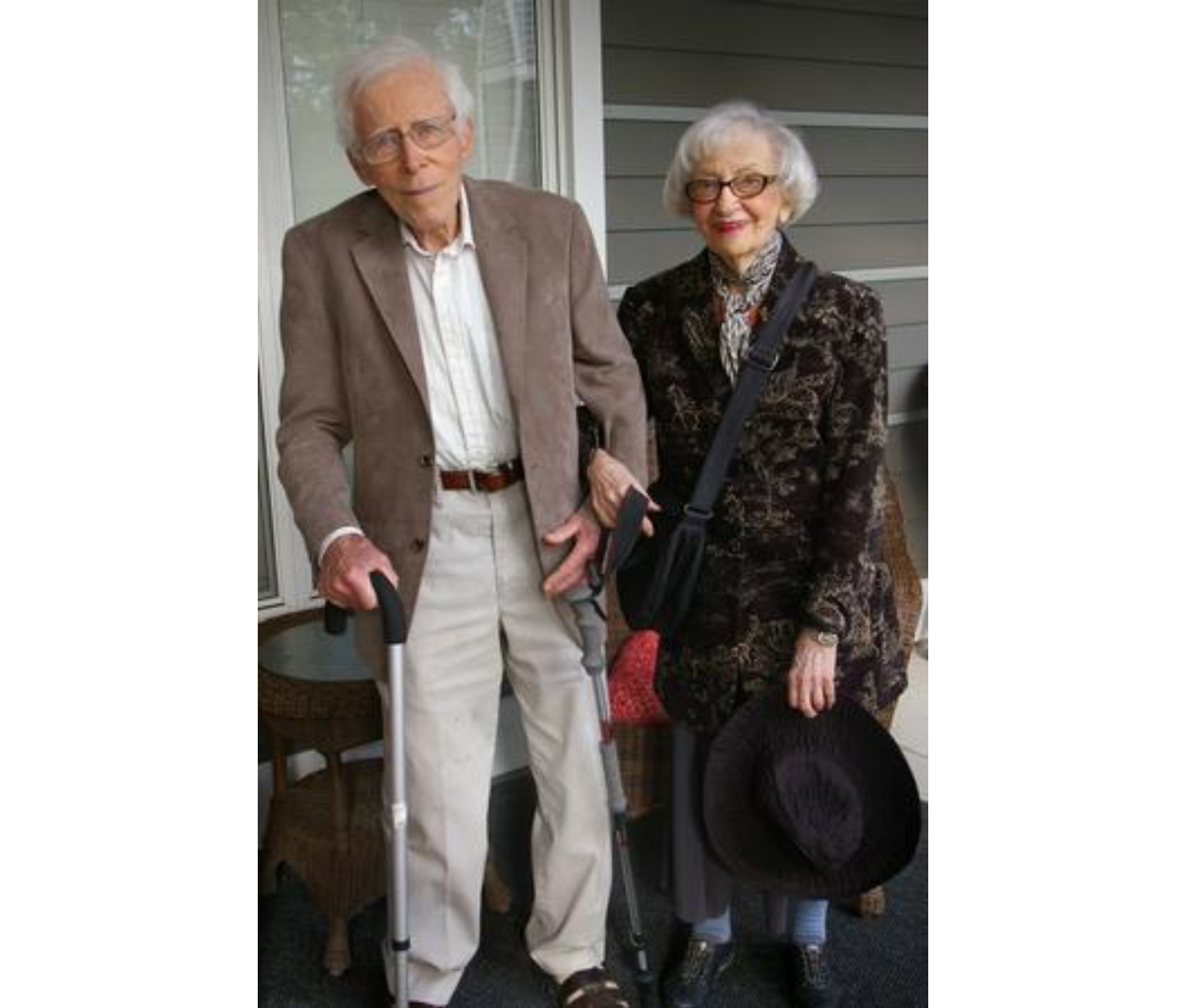 An image of an older man and older woman standing in front of a house. They are both holding canes and smiling at the camera.