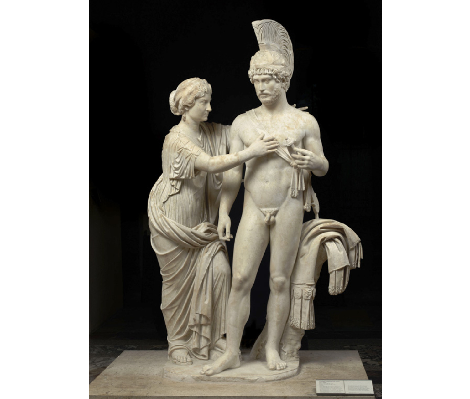 Statue of a man wearing a helmet and a woman, her arms reaching around the man, dressed in draped robes.