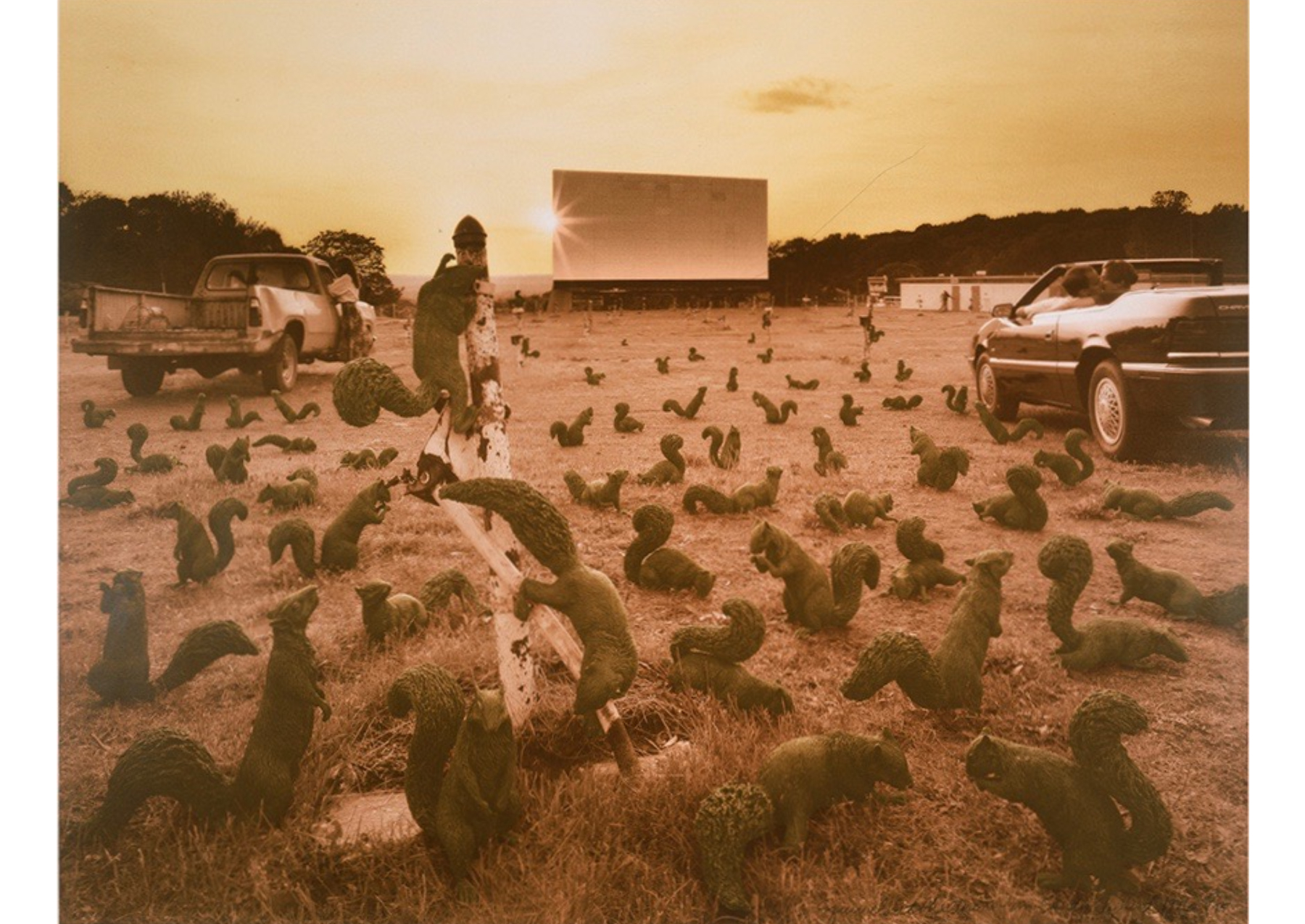 Sepia-tone photo of hundreds of squirrels at a nearly-empty drive-in movie theater at sunset.