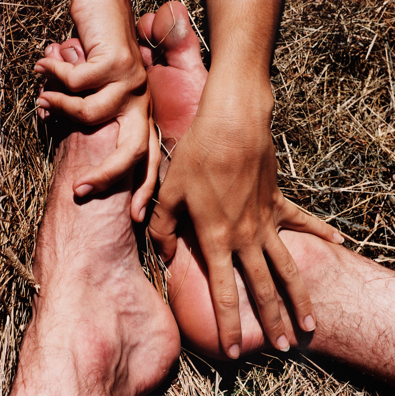 Photograph of two hands touching two feet on the ground.