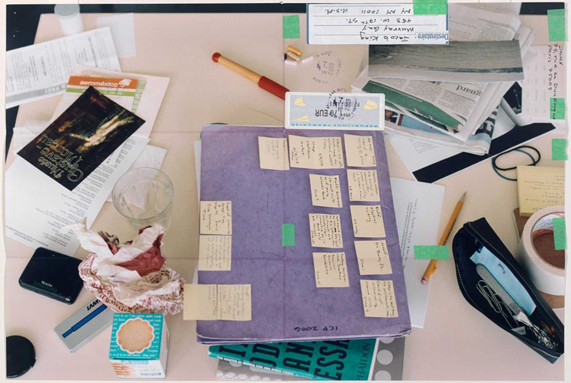 Close-up of table top with piles of papers, crumpled paper, purple file folder covered in small yellow post-it notes, empty glass, newspaper, subway card, masking tape, two rubber bands, pen and mechanical pencil, and Musee Gustave Moreau ticket; bits of tape and cancelled stamps, addressed to Jacob King / Murray Guy / 453 W. 17th street / NY NY 10011 / USA from Davey 74, rue de Dunkerque 4 g / Paris 75009