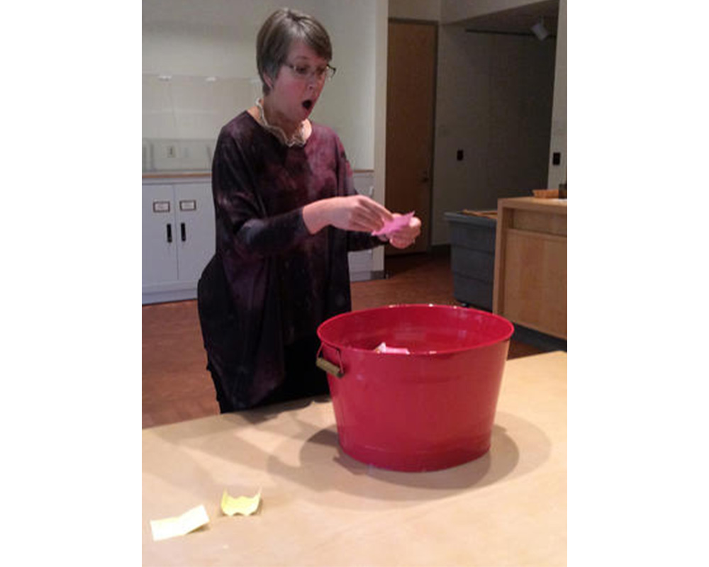 woman pulls a slip of paper out of a red bucket with surprised expression in her face