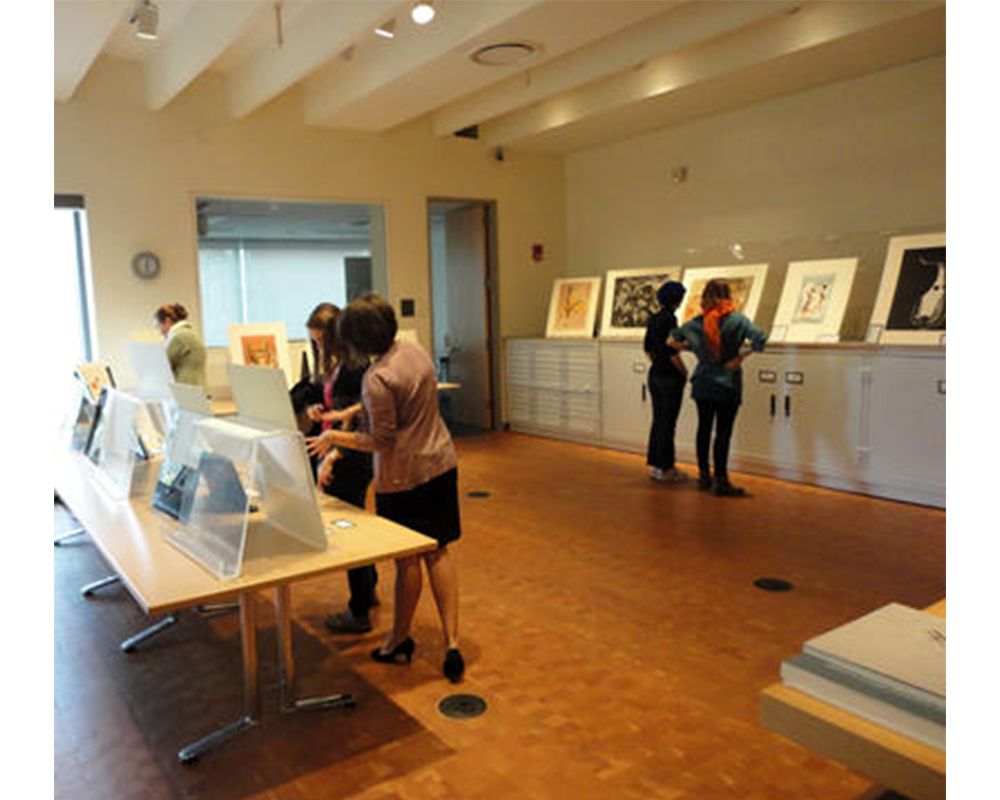 students standing in an art gallery. prints propped up on a table and on a cabinet