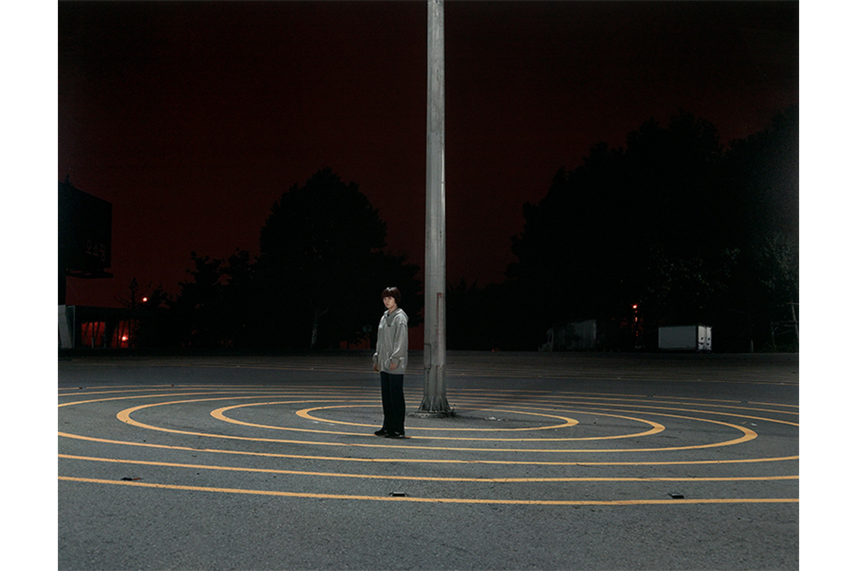 night, boy standing near a pole in the center of a series of yellow concentric circles