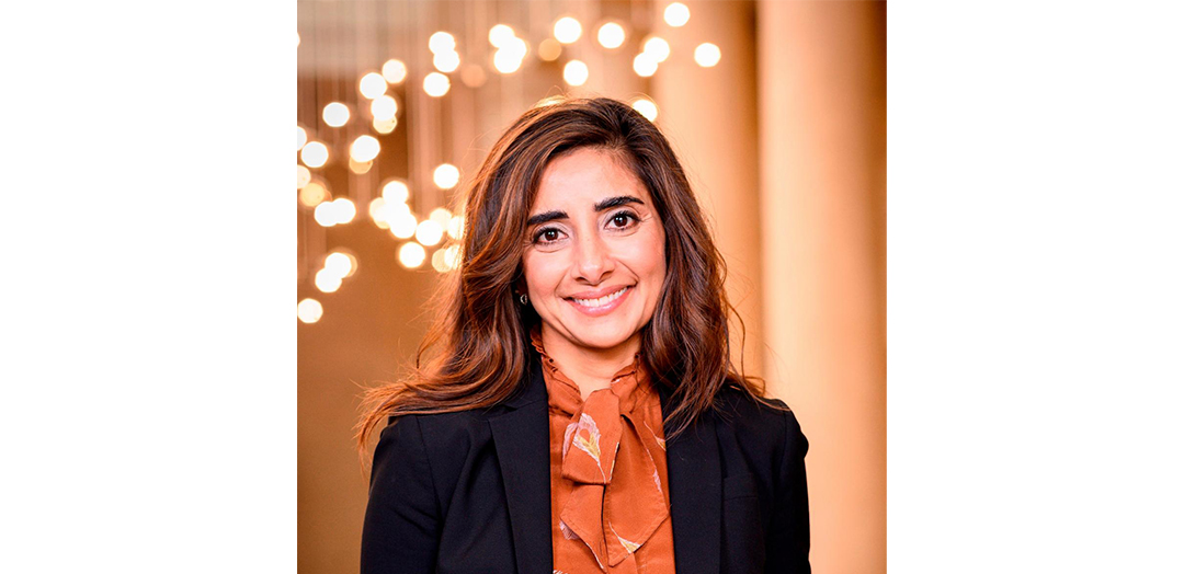 Headshot of Asma Naeem, she is smiling and wearing an orange blouse and black blazer. 