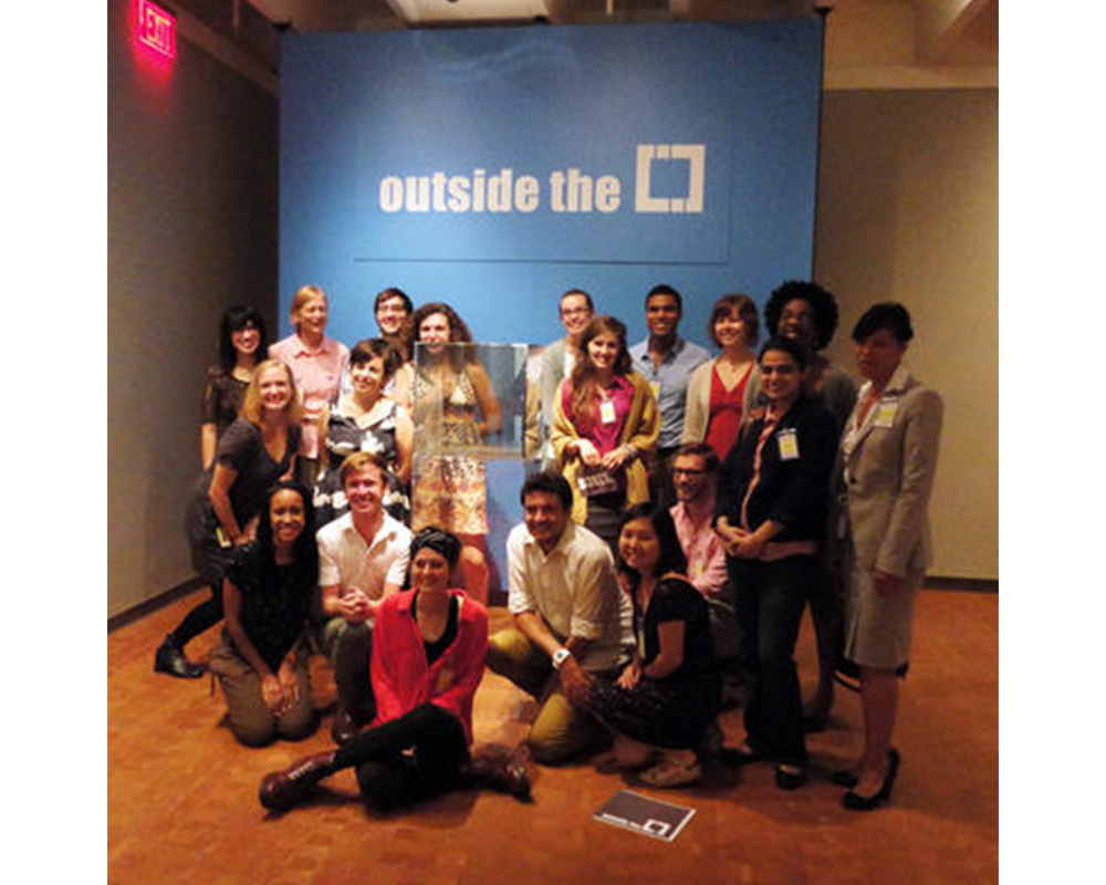 nineteen students standing in front of a blue wall with white text that says "outside the [box]"