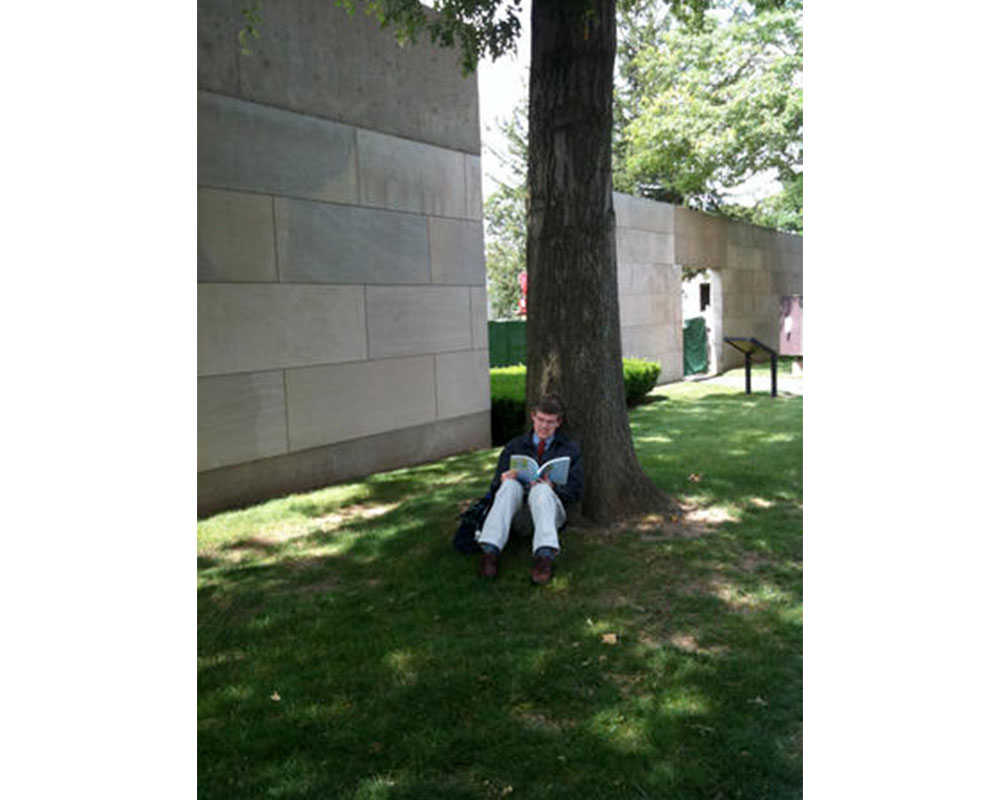 man sitting on grass under a tree, reading a book