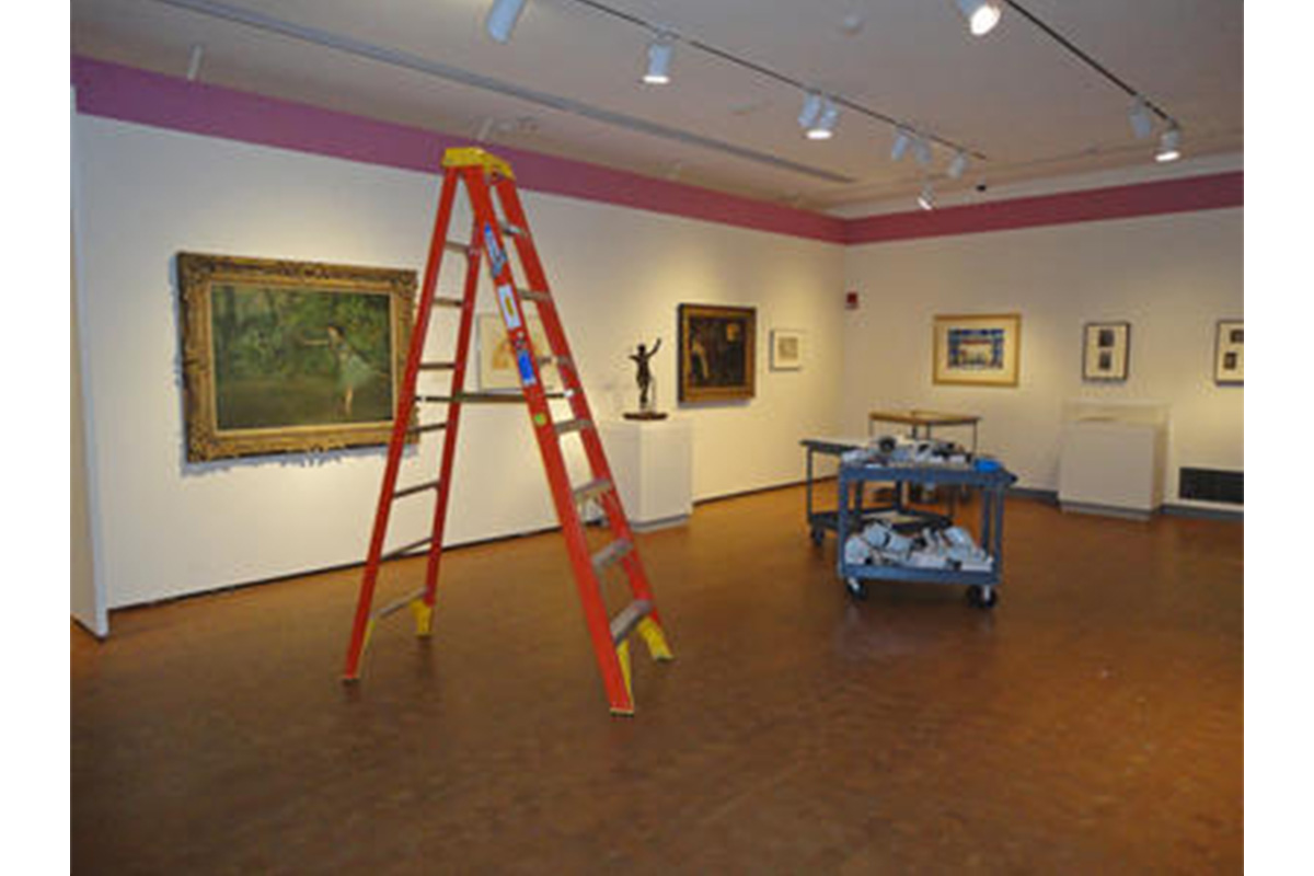 gallery with artworks displayed on the walls, orange ladder and blue cart in the middle of the gallery