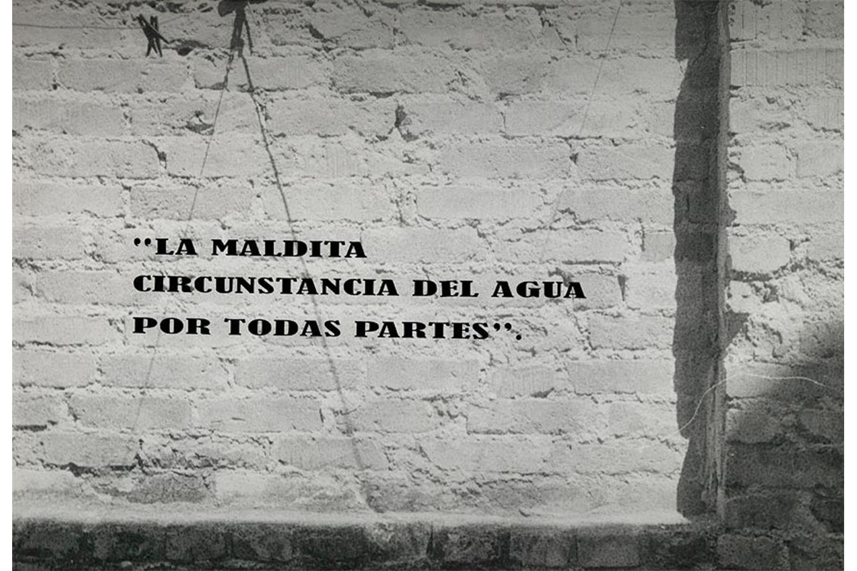 brick wall with indentation and applied text: 'LA MALDITA / CIRCUNSTANCIA DEL AGUA / POR TODAS PARTES".