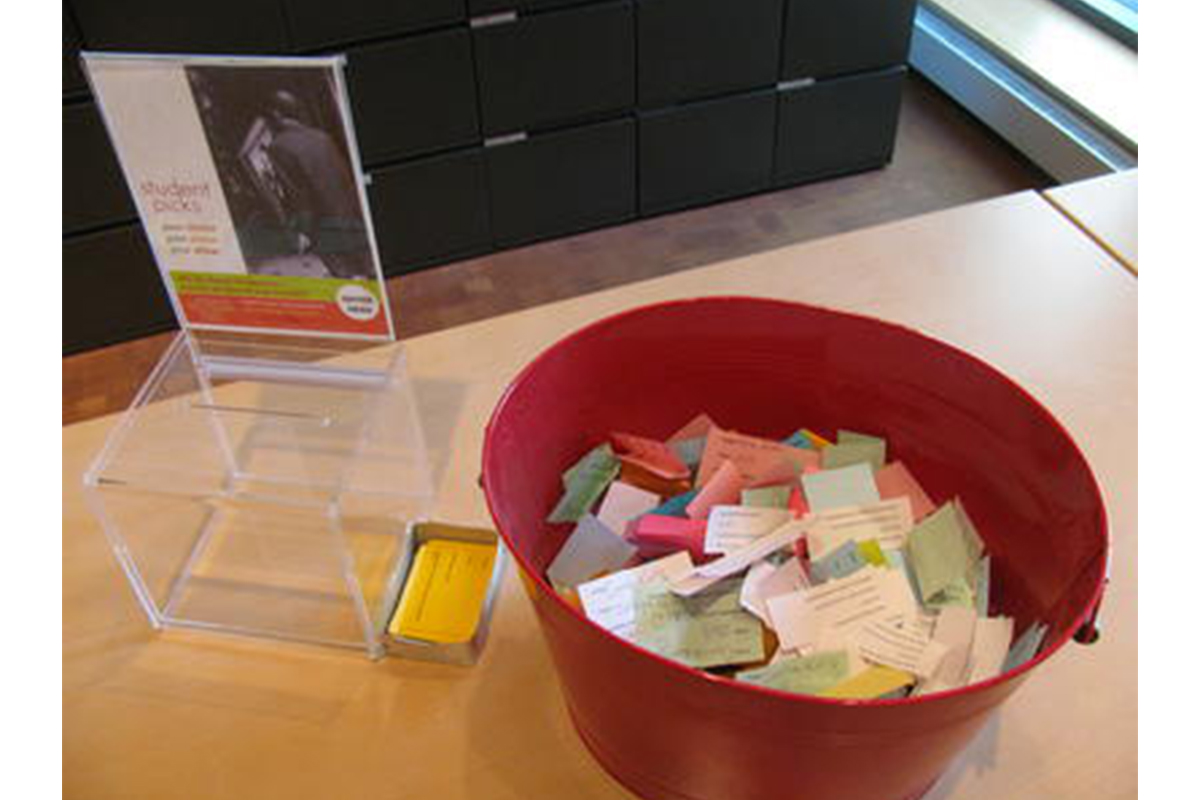 wooden table with a red bucket on it, full of colorful slips of paper