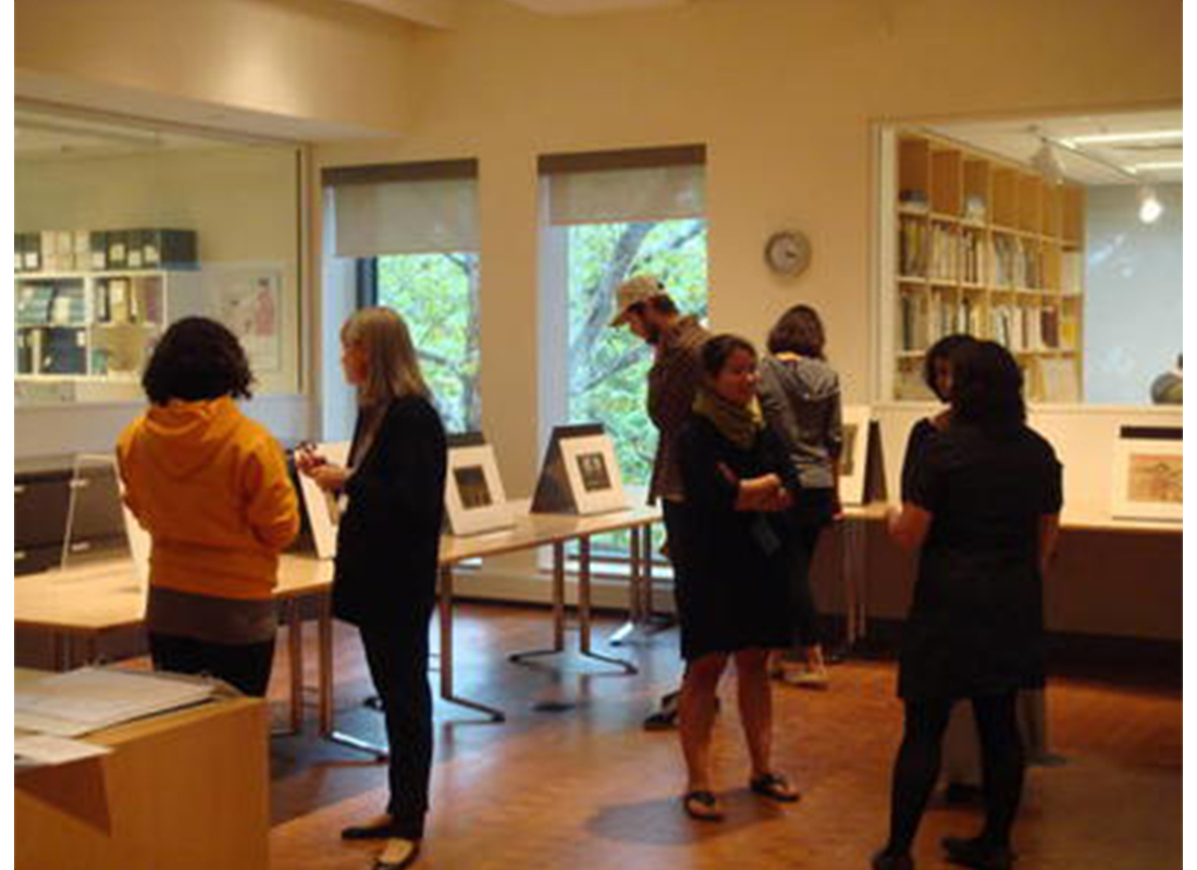 room with tables with printed propped up on them; people stand looking at the prints