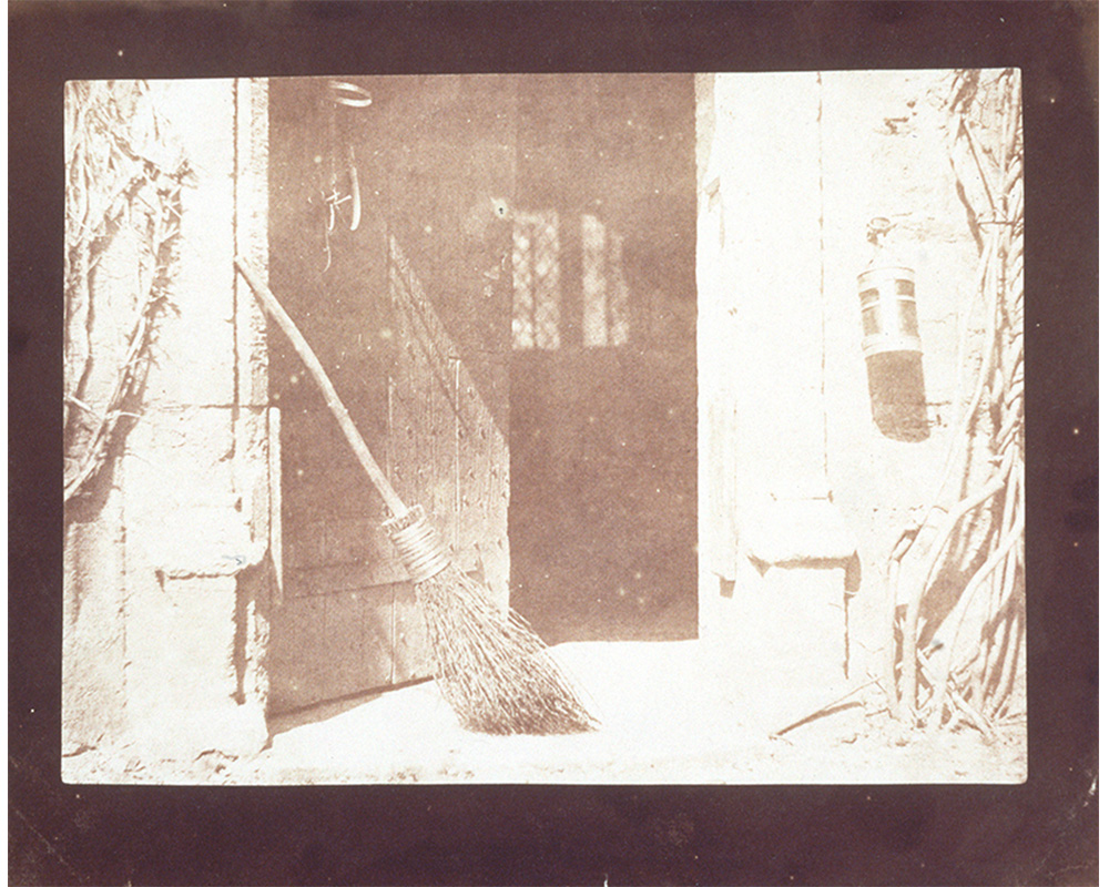 open doorway of a barn with broom resting against a wall on the left, lantern hanging on a wall on the right