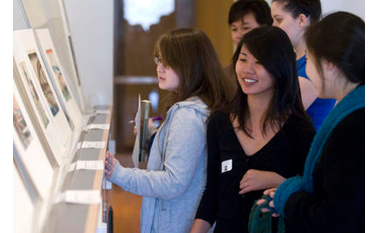 group of students stands looking at a display of prints propped up on a tabletop