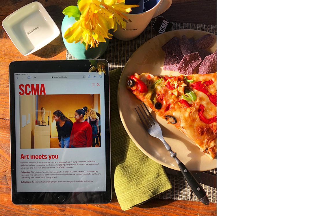 Image of an IPad looking at SCMA on a desk with yellow flowers and a slice of pizza on a plate.