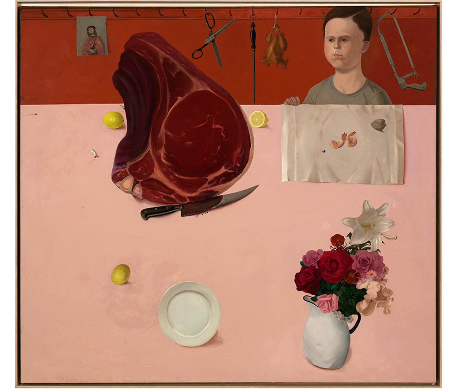 boy standing at pink tabletop observing a collection of items on the table: cut of meat and bloody knife, lemons, plate, white pitcher holding flowers, and two shrimp and a clam on a white napkin. Behind him, a portrait of Jesus, a pair of scissors, a knife steel, a chicken, and a saw hang on a row of hooks.