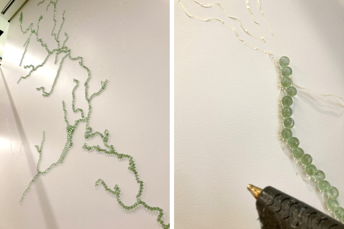 left: view from below of trails of blue-green marbles on the white wall; right: a glue gun in front of a short line of marbles on the wall and lines of thin white tape marking their progression