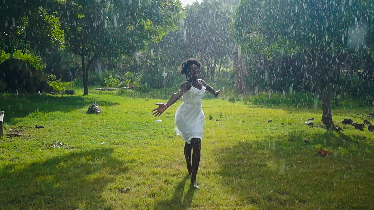 young black girl wearing a white dress, smiling, runs through the rain with arms outstretched and the sun shining