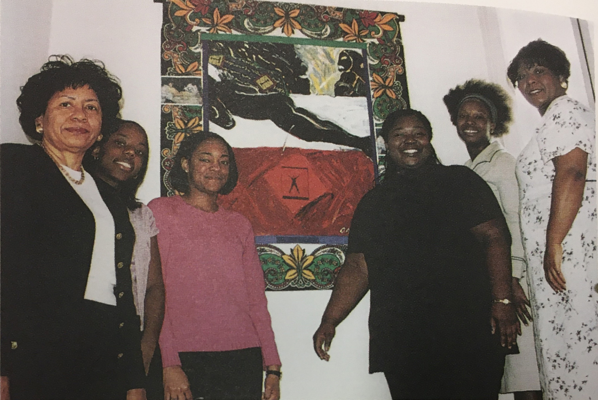 Six smiling Black women stand in front of One Who Watches