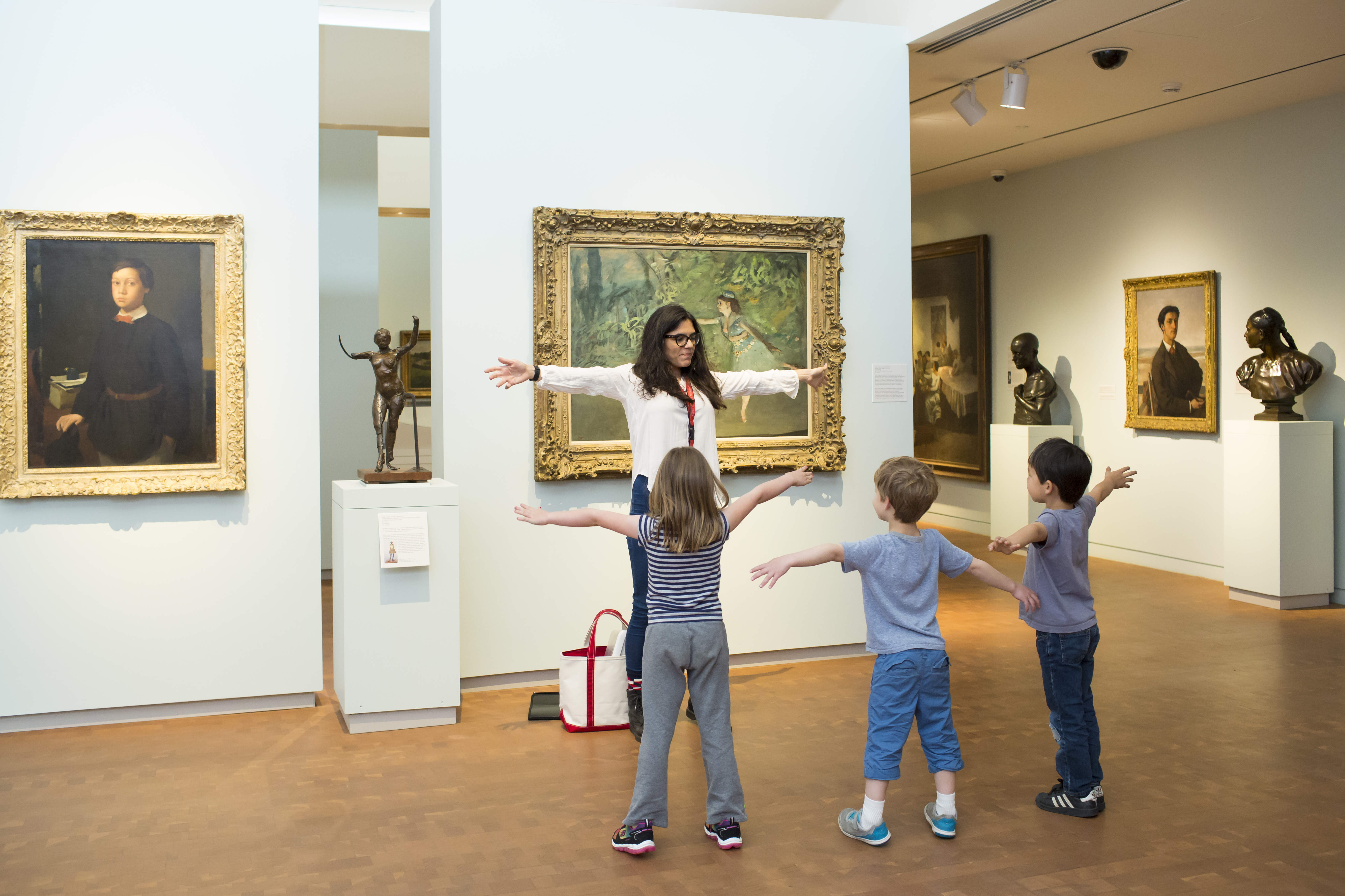 Museum educator in front of paitning with young kids, mimicking the figure in the painting