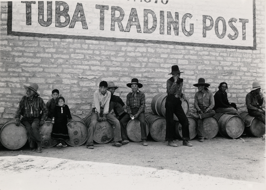 "Men and children seated on barrels under a sign that reads "TUBA TRADING POST""