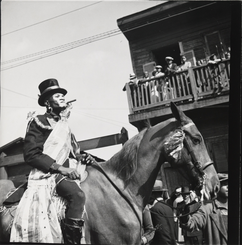 "Black man wearing top hat on a horse lower left; people watching from a balcony upper right"