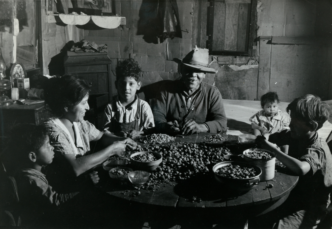 "man, woman and four children seated around a table shelling nuts"