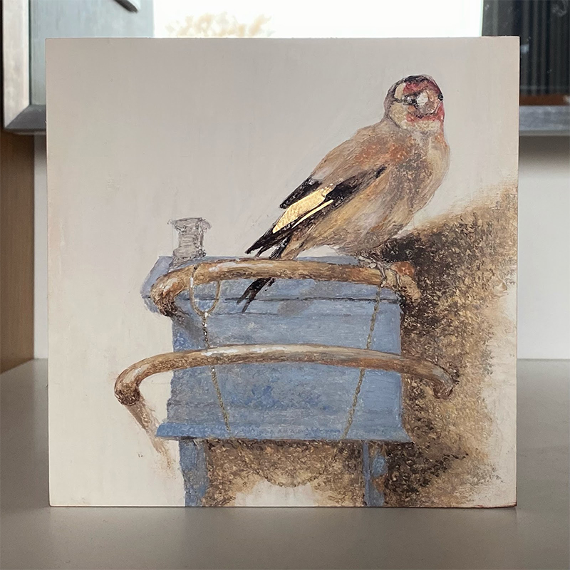 goldfinch sitting atop a pastel blue bird house on a white background