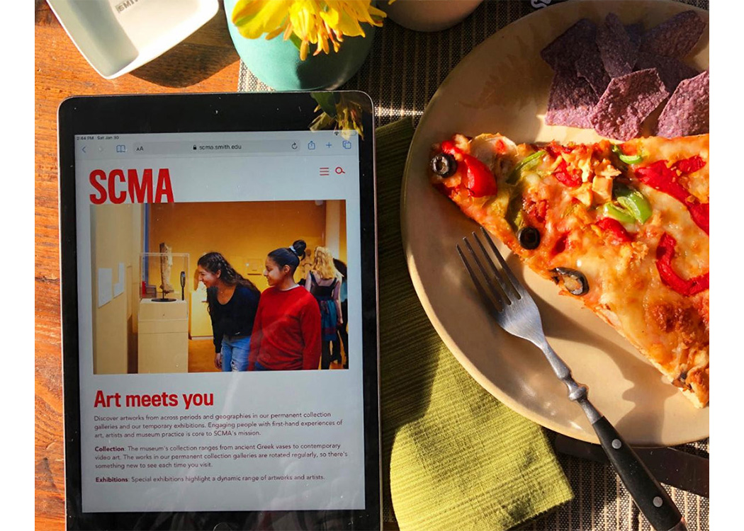 Photo of ipad with SCMa website on screen with pizza to the right and flowers at the top of the image, all on a table