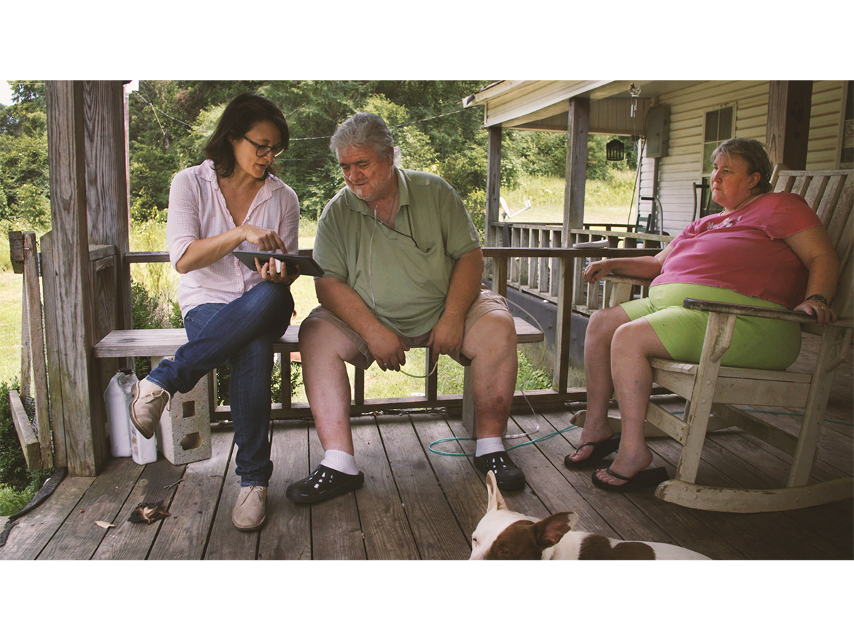 Two women and a man sitting on an outdoor porch with one man and woman looking at an iPad
