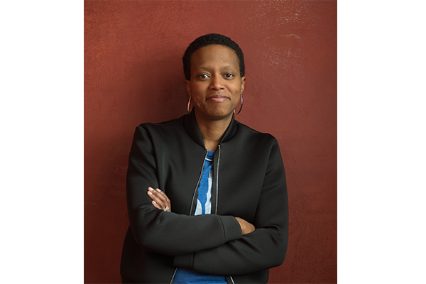 Torso photo of artist Amanda Williams in a dress coat leaning against a dark red wall