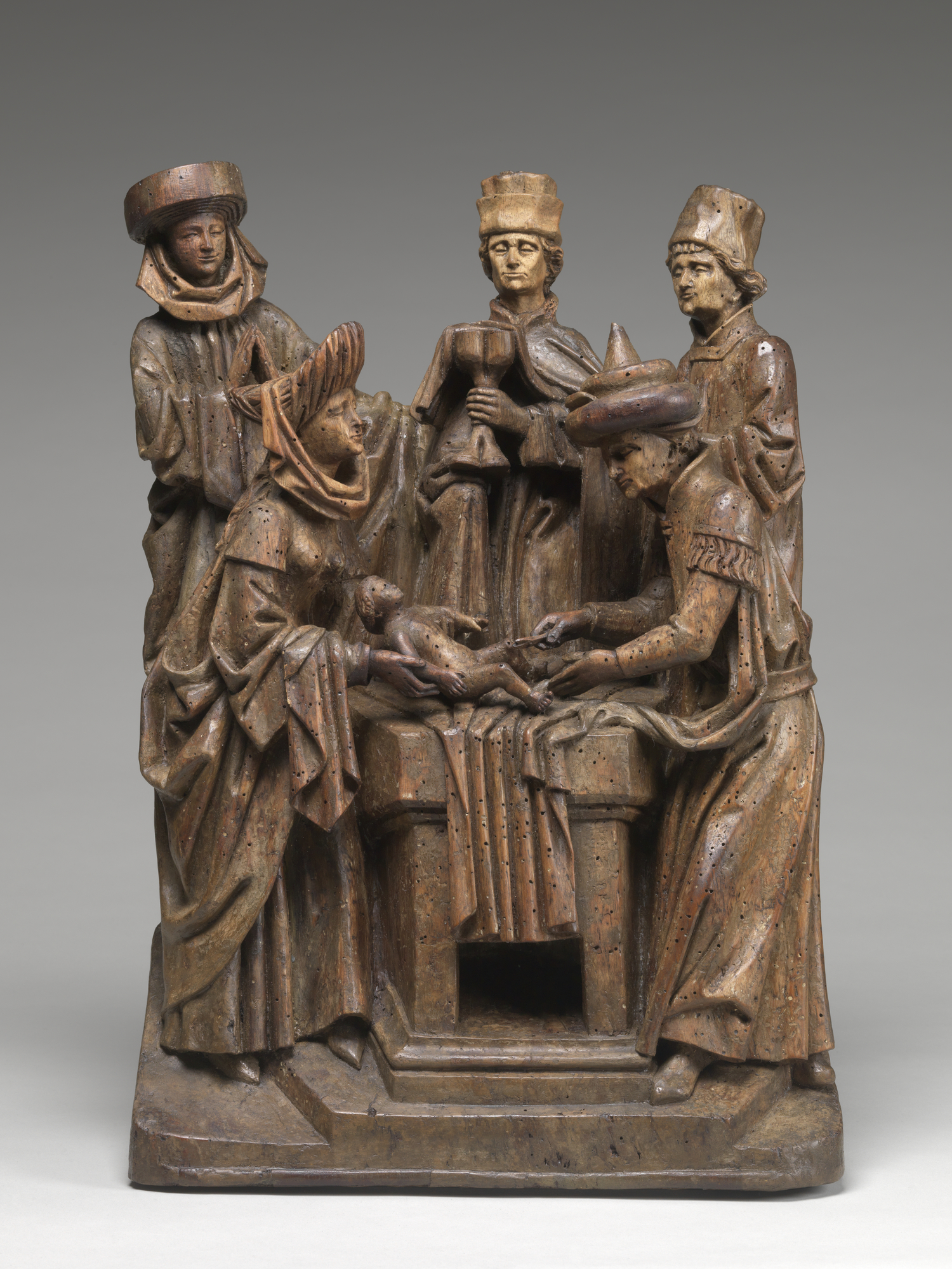 Wooden sculpture representing a crowd of men observing a circumcision. 