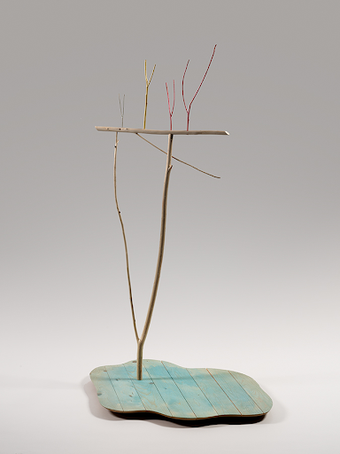 Image of a sculpture by Truman Lowe, depicting a turquoise organic flat shape with a long thin branch sticking straight out of it.
