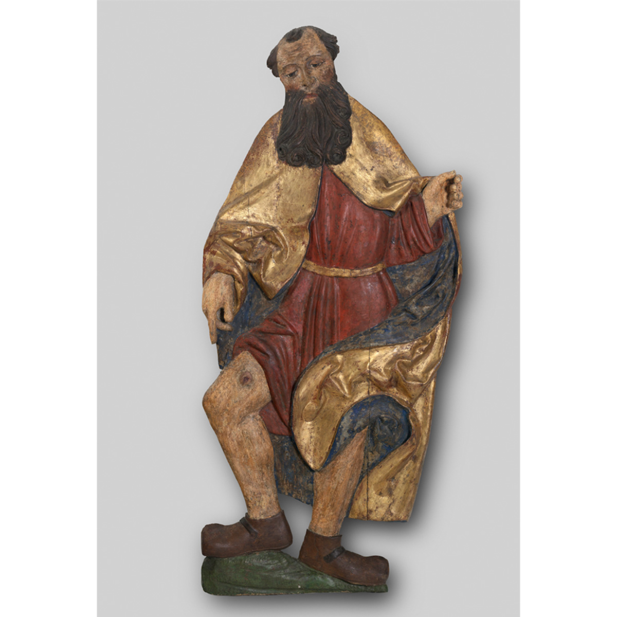 Painted wooden sculpture of a front facing jolly man in red and gold robes.