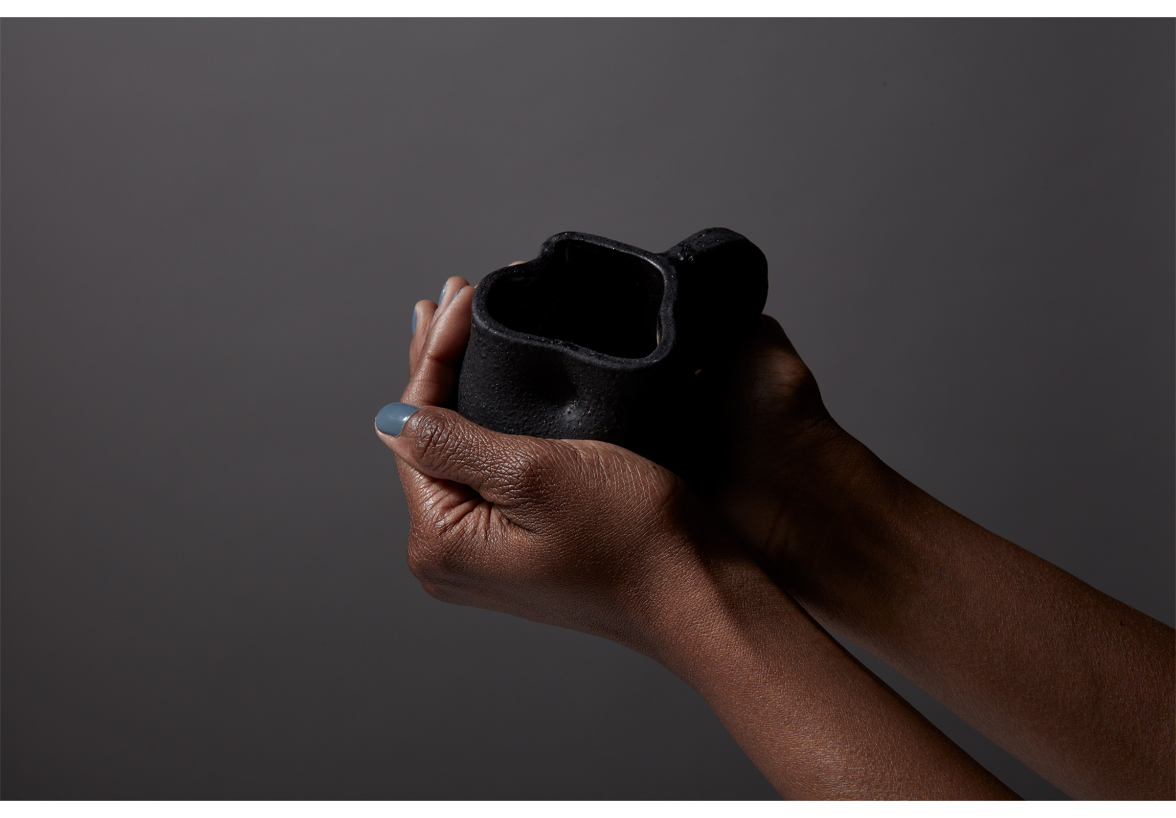 set of hands with forearms holding fingers around a black glazed mug