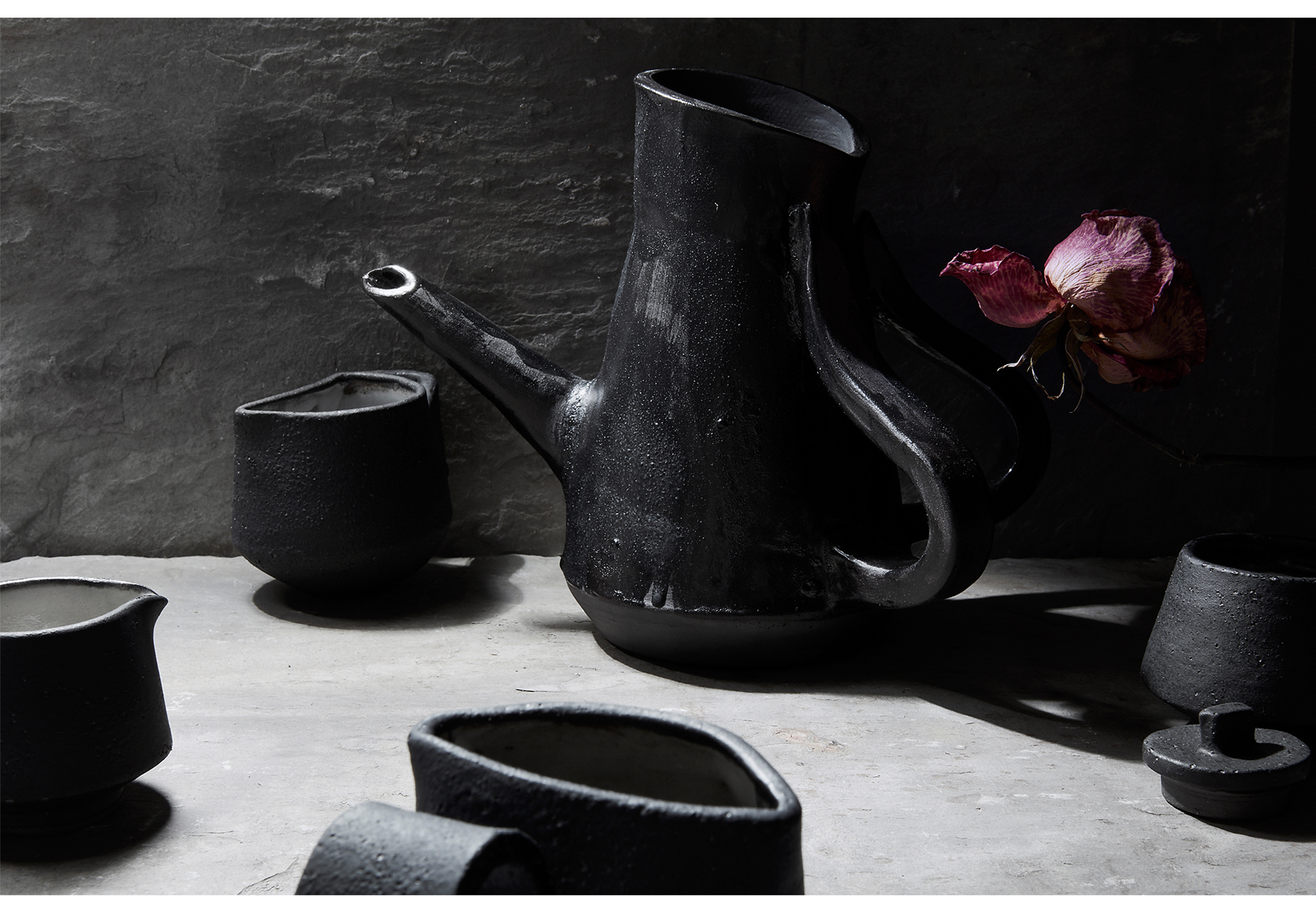 Set of black glazed teapot surrounded but hand made unique hand-sized teacups