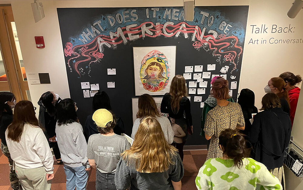 Bird's eye view of a group of students in front of a wall with the chalked words: What Does it Mean to be American?