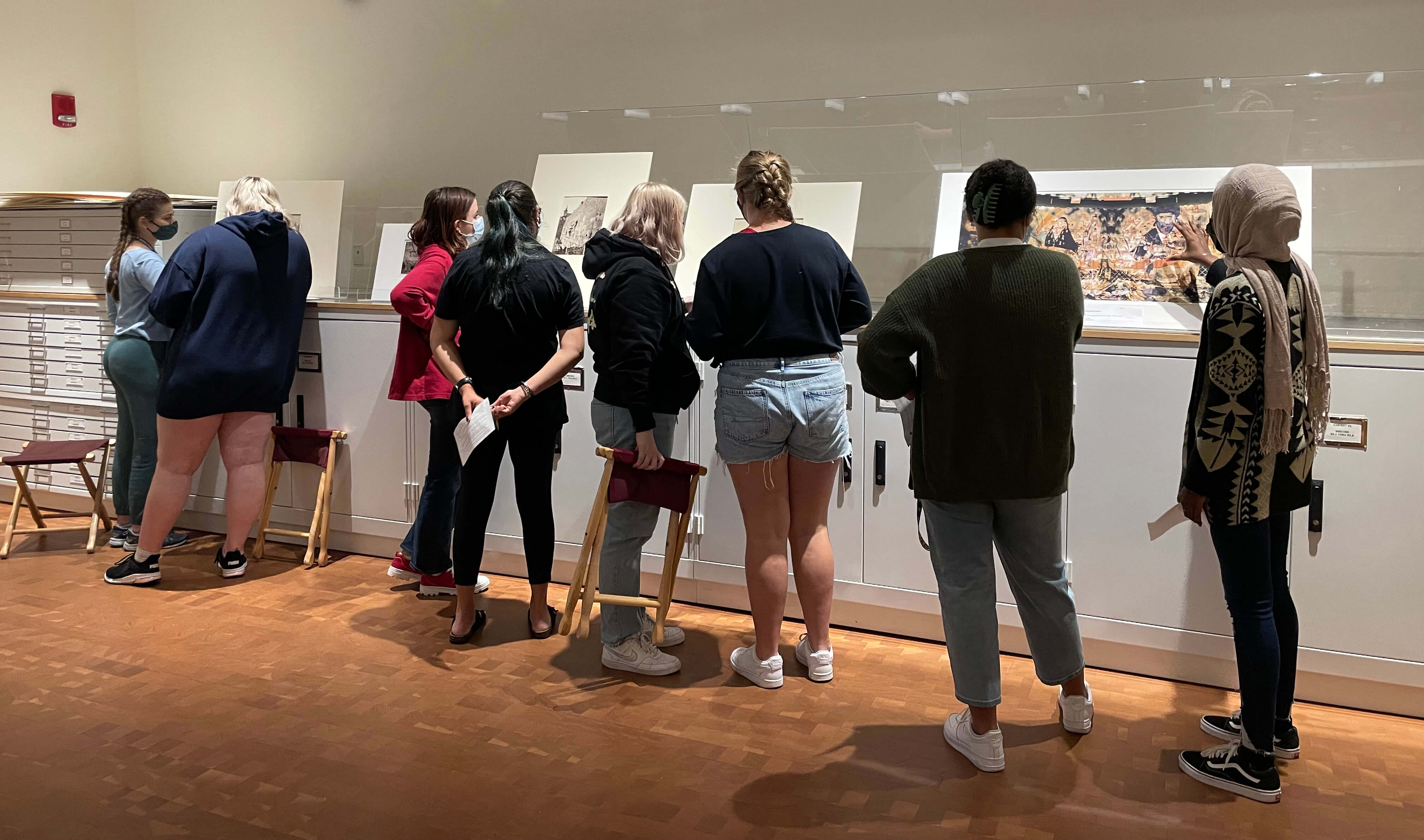 Eight students looking at artworks lined up on a counter