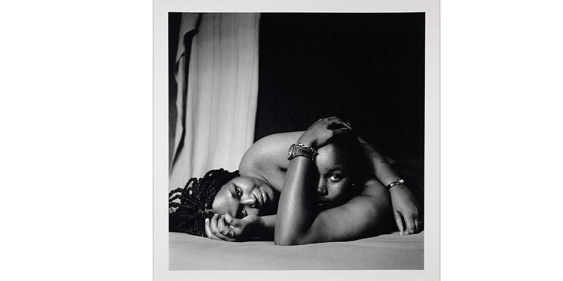 Black and white photo of two women laying down together on a mattress, heads and naked shoulders in view only
