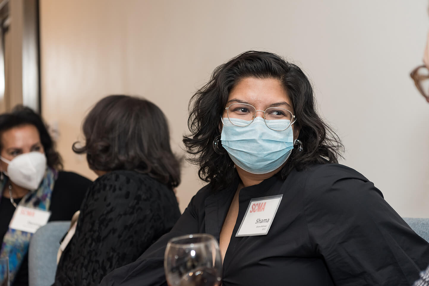 Woman in glasses and shoulder length hair turning towards camera with a blue mask on