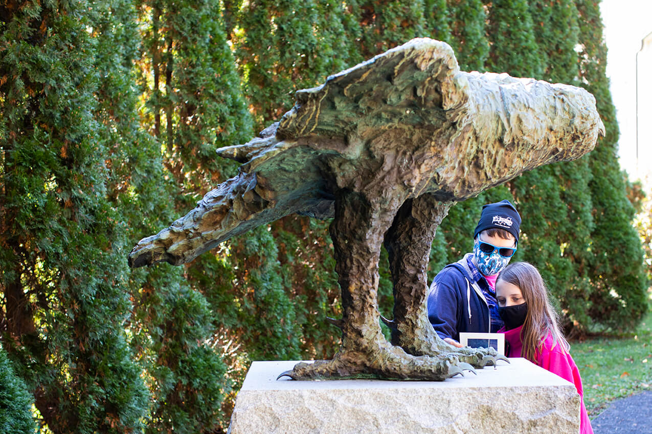 Large outdoor owl sculpture with woman and young child standing behind the sculpture looking at it.