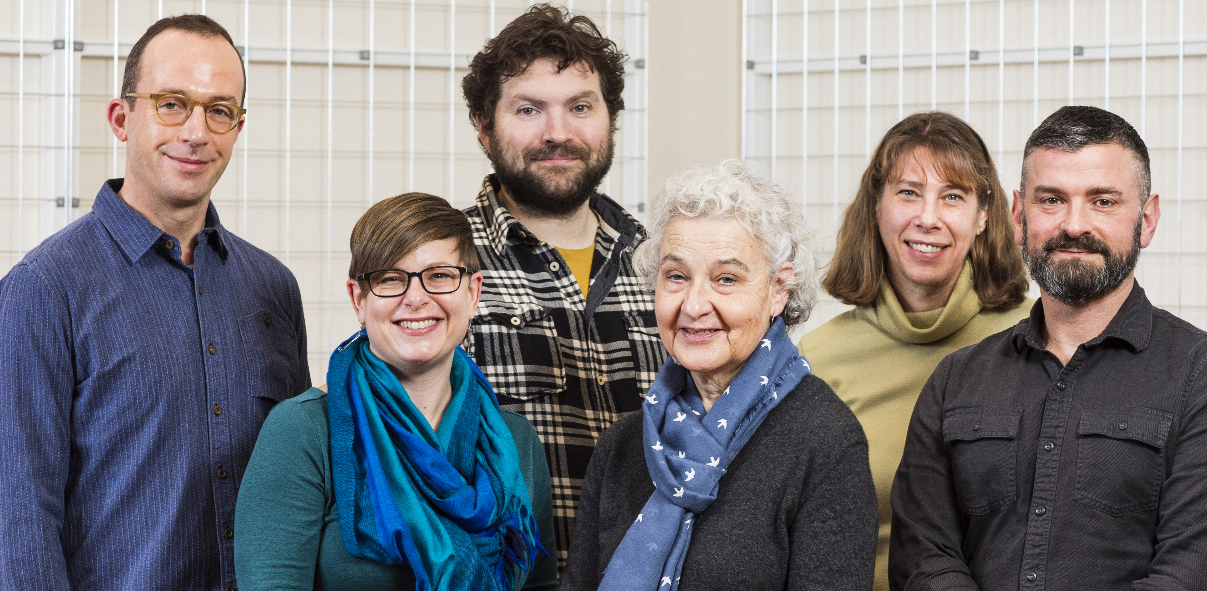 Six people of varying heights standing for a photo and looking at camera