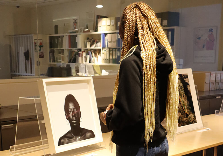 Student with long blond braids standing in front of a table looking down at a black and white photograph of a person's shoulders and head